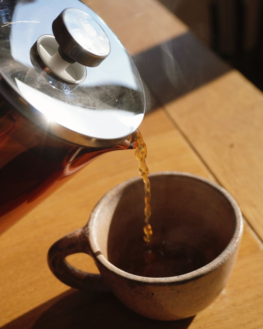 Fresh coffee pouring from a glass French press into a ceramic mug