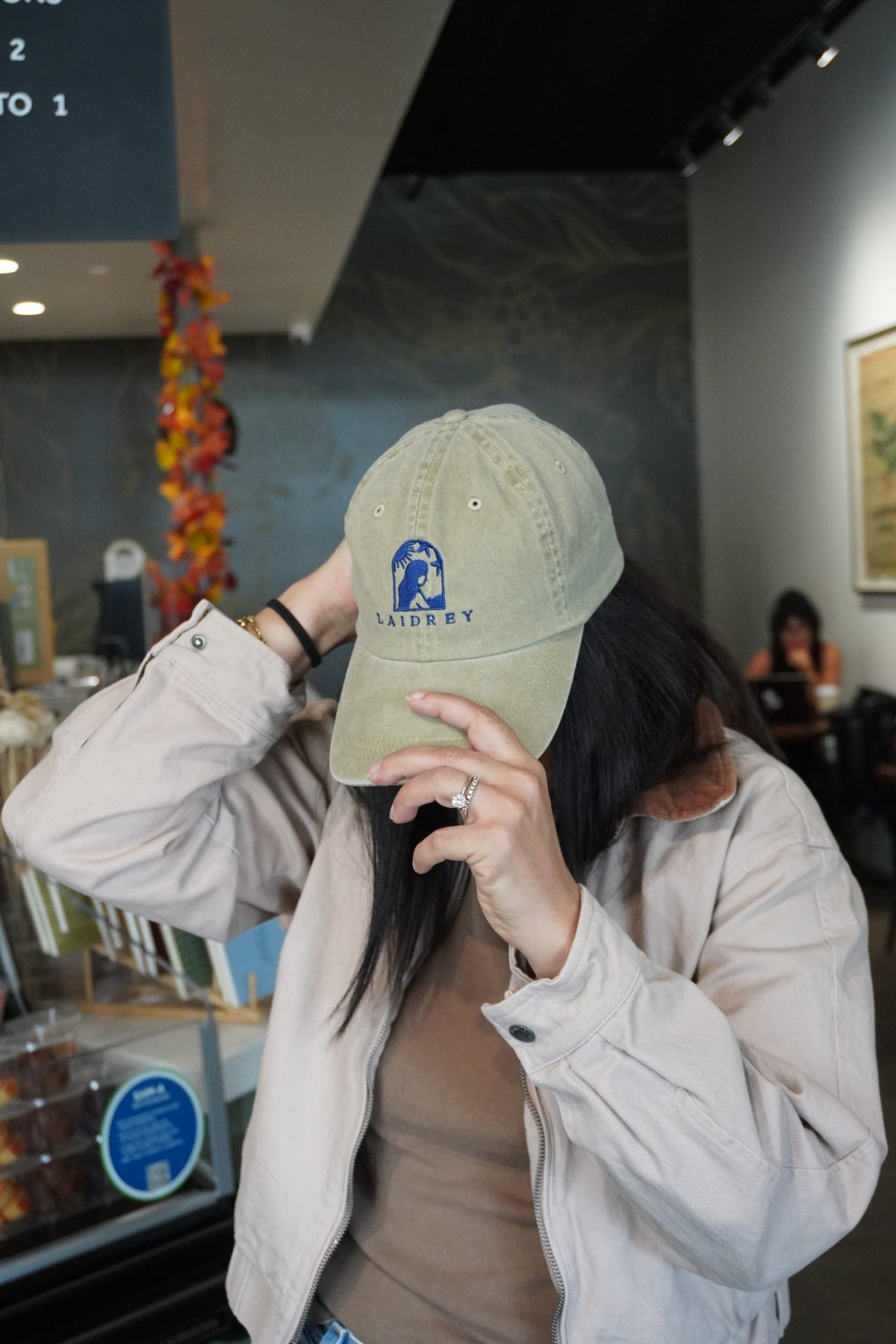 Woman adjusting the curved visor of a beige Laidrey baseball cap with an unstructured, low-profile fit