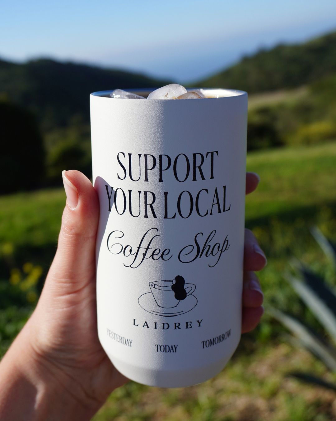 Reusable coffee tumbler being held with support your local coffee shop design